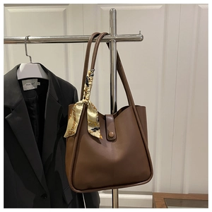Detail of dark brown leather tote bag with printed silk scarf handle and metal snap closure