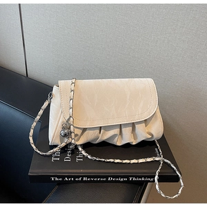 Detail view of cream ruched crossbody bag with silver charm and chain strap on book