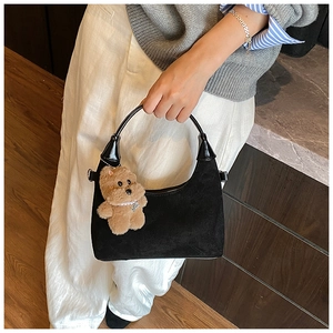 Detail of black suede hobo bag featuring a cute brown plush bear charm with pearls