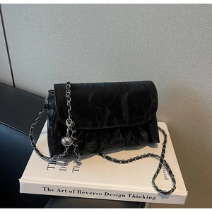 Detail of black pleated chain crossbody bag with silver sphere pendant on a book