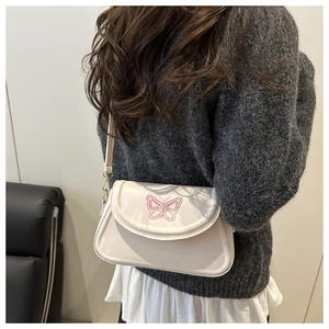 Detail of cream white shoulder bag featuring pink butterfly embroidery and flap closure