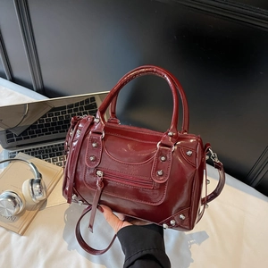 Sac Boston rétro en cuir verni bordeaux avec rivets et glands sur bureau de travail