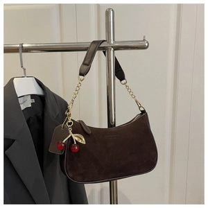 Detail of dark brown suede shoulder bag with gold chain and cherry charm accessory