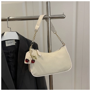 Detail of cream hobo bag with cherry charm and gold chain strap on black blazer
