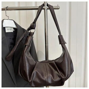 Close-up of dark brown leather pleated dumpling bag with knotted strap and metal rings