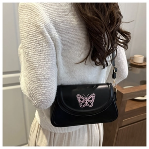 Detail of pink butterfly embroidery on black leather flap bag worn by a model