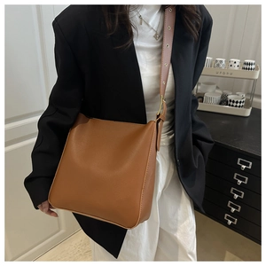 Detailed view of the brown leather bucket bag with adjustable strap worn by a model