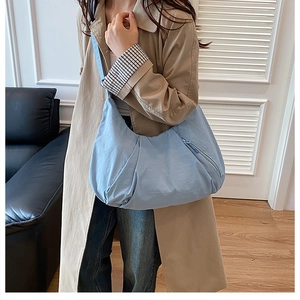 Light blue pleated tote bag with wide strap worn by a model in a minimalist home setting