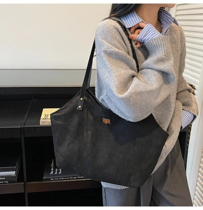 Detail of black suede tote bag with golden twist lock and rivet accents on shoulder strap