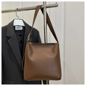 Detail of deep brown leather bucket bag featuring wide strap and golden metal buckle