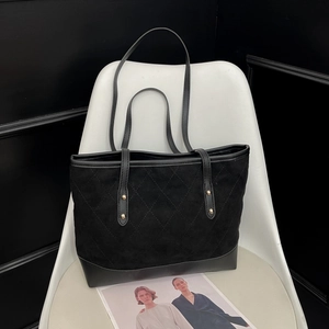 Sac fourre-tout matelassé en velours avec base en cuir noir et rivets dorés sur chaise