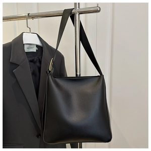 Detail of minimalist black leather bucket bag with gold hardware on office attire