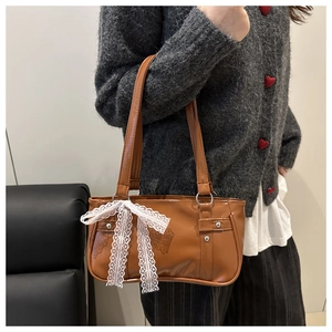 Detail of brown glossy PU leather bag with white lace bow and rivet accents on strap