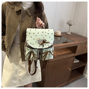 Detail view of mint green backpack featuring star patterns and brown ribbon bows