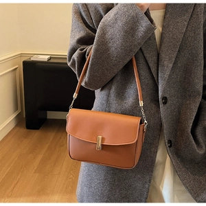 Detail of caramel crossbody bag with gold rectangular buckle on a minimal indoor model