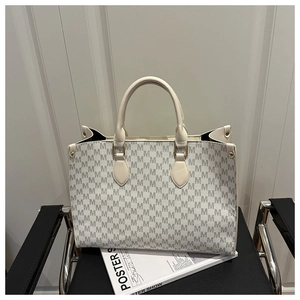Close-up of cream tote bag with grey M monogram pattern on a modern black chair