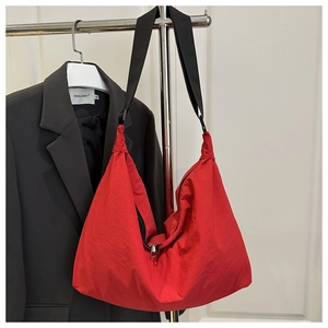 Detail of red nylon tote bag with pleated texture and black strap on a hanger