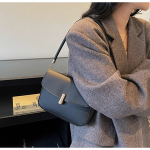 Detail of a chic black leather crossbody bag with a sleek gold metal bar buckle on gray blazer