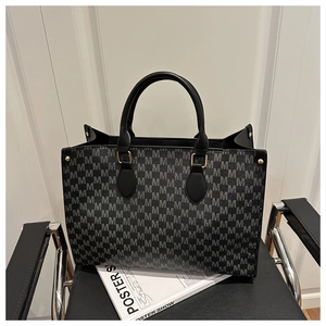 Detailed close-up of a black tote bag with gray M-letter pattern and gold metal hardware