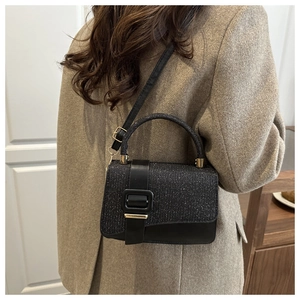 Detail of a chic black crossbody bag with sparkling rhinestones and a gold buckle on a coat