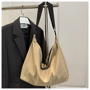 Detail of beige crescent tote bag with wide black strap and dual metal zippers