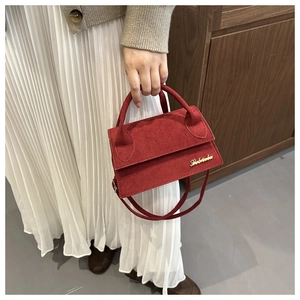 Detailed close-up of a vibrant red suede mini handbag with gold logo and crossbody strap