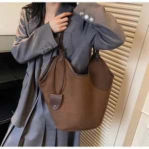 Detail of a large brown suede tote bag with contrast leather trim on a model's shoulder