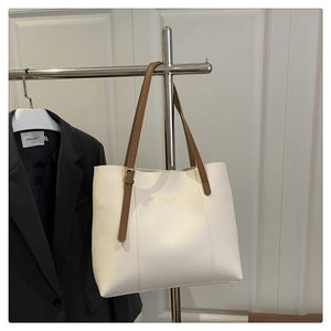 Detail of cream white tote bag with brown leather straps and adjustable gold metal buckle