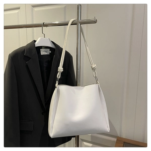 Detail view of white leather shoulder bag with artistic knot handle and trapezoid structure