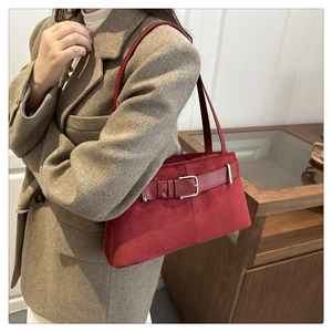 Detail of red suede shoulder bag with buckle strap on a camel wool coat background