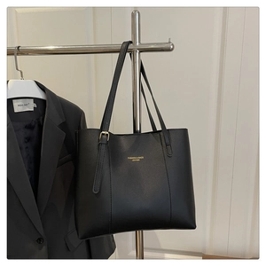 Detail of minimalist black leather tote bag with gold lettering and decorative buckle