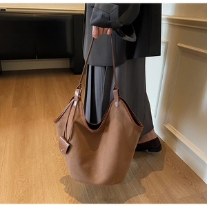 Close-up of suede tote bag with contrast charm and leather shoulder strap detail