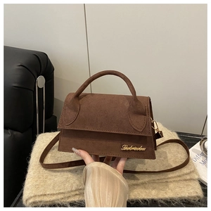 Detail of deep brown suede-textured small square bag with elegant gold logo on beige fabric
