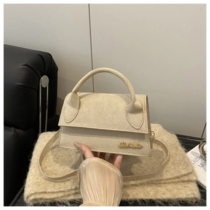 Detail of beige suede crossbody bag with gold logo on soft fabric background