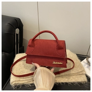 Detail of red faux suede handbag with gold metal logo on a beige knit fabric texture