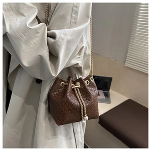 Detailed view of brown woven bucket bag with pearl charms and golden metal chain strap