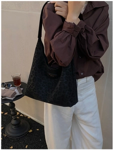 Detail of black leopard print hobo bag with leather logo tag on brown shirt background