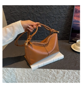 Detail of brown lychee grain leather bag showing knotted handle and top zipper closure