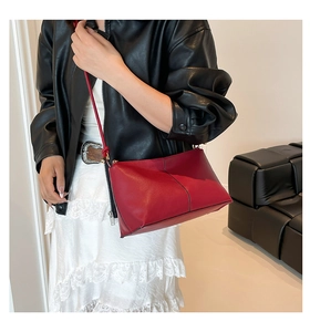 Detail of red leather crossbody bag with black contrast stitching worn by a model
