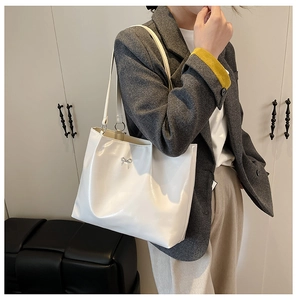 Close-up of white glossy faux leather tote bag with metal bow detail on a shoulder strap