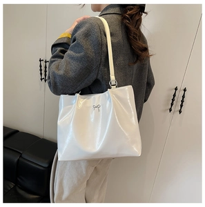 Close-up of white patent leather tote bag featuring a decorative silver metal bow accent