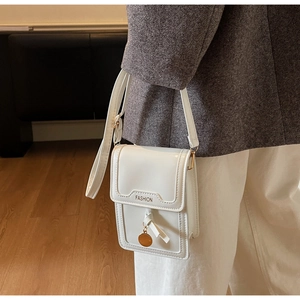 Detail einer weißen Mini-Umhängetasche mit goldenem Fashion-Schriftzug und Quaste am Model