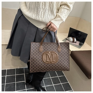 Detail of a brown tote bag with M letter monogram print and leather embossed round logo
