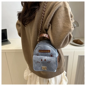 Detail of a mini denim backpack with cat ears and gold chain strap worn by a model