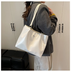 Detail shot of a large white glossy tote bag featuring a silver bow metal accessory