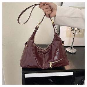 Detail of burgundy patent leather hobo bag featuring gold zipper and adjustable strap