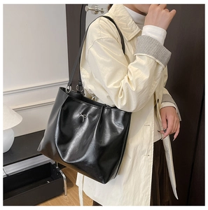 Detail of black faux leather tote bag with silver bow accent and elegant pleats