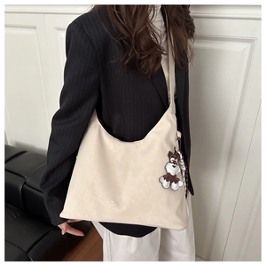 Détail d'un sac cabas beige à texture souple avec un pendentif décoratif en forme de chien