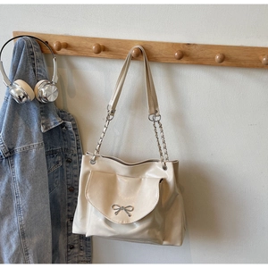 Close-up of beige tote bag featuring metal bow buckle and leather chain shoulder strap