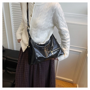 Detail view of a black patent leather hobo bag with gold hardware and side zipper pockets